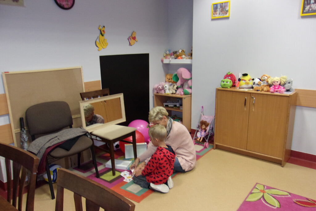 Dziecko w czerwonej bluzie bawi się z kobietą w pokoju pełnym zabawek