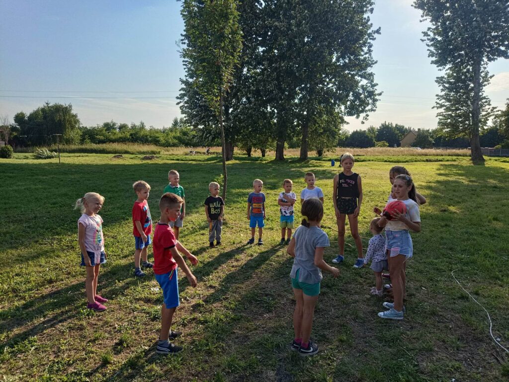 Czternaścioro dzieci bawi się na trawiastej murawie piłką