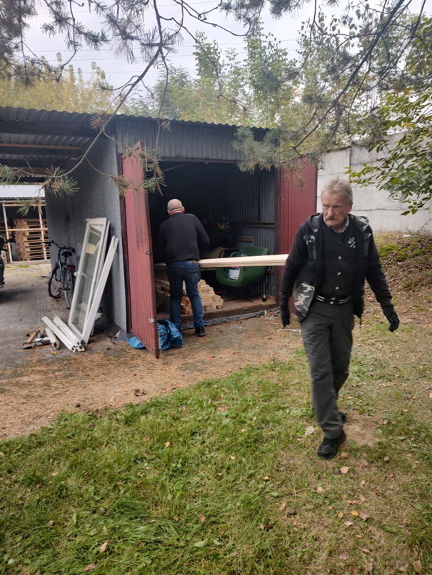 Na zdjęciu dwóch mężczyzn przygotowujących materiały do wykonywania prac związanych z działaniami w warsztacie stolarskim. Zdjęcie obrazuje zaangażowanie i wysiłek mężczyzn w czynności związane z warsztatem stolarskim.